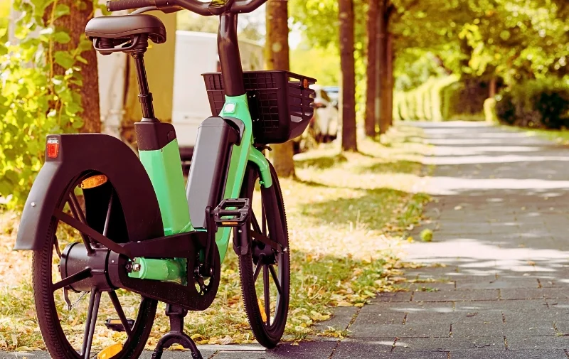 A light green electric bicycle parked on a sidewalk.