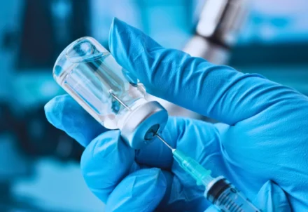 Gloved hand drawing liquid from vial into a syringe.