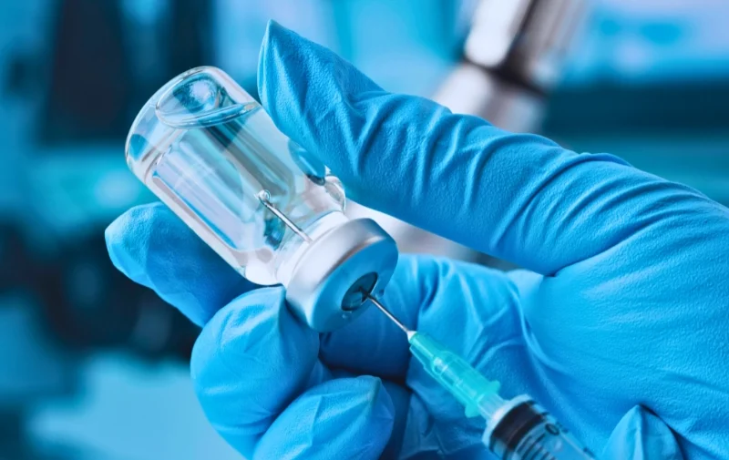 Gloved hand drawing liquid from vial into a syringe.