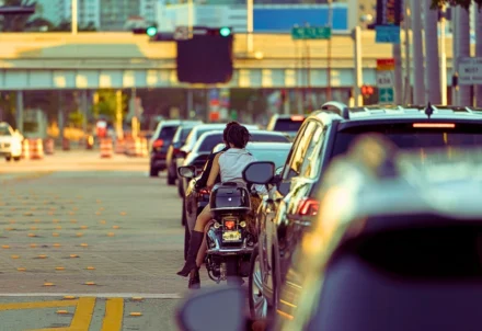 Two people on a motorcycle wait in city traffic.