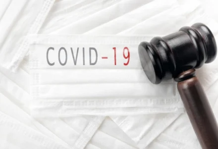 A wooden judge's gavel resting on white medical masks.