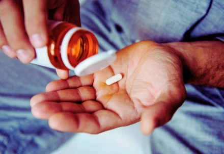 Person pouring a single white pill into their palm.
