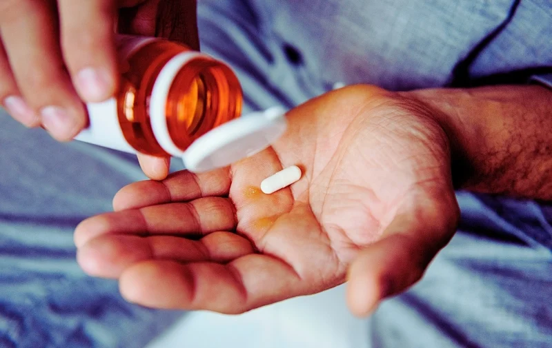 Person pouring a single white pill into their palm.