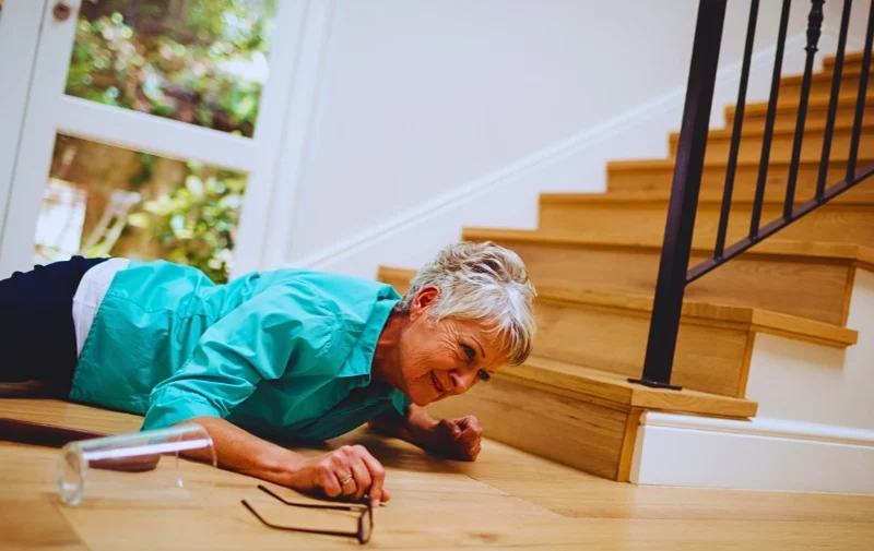 An elderly woman fallen on the floor near stairs.