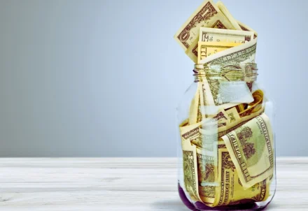 A glass jar overflowing with American dollar bills.