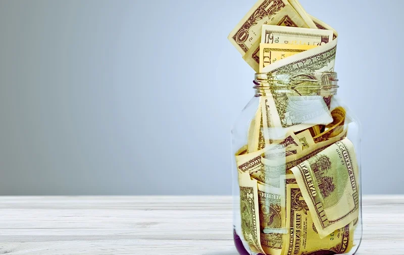 A glass jar overflowing with American dollar bills.