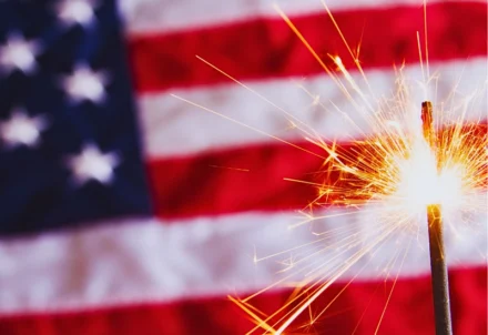 A sparkling handheld firework in front of an American flag.