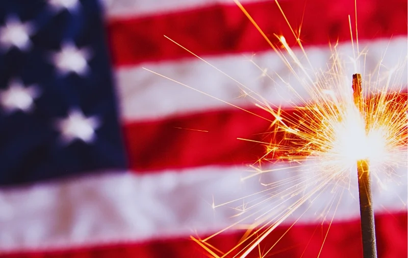 A sparkling handheld firework in front of an American flag.