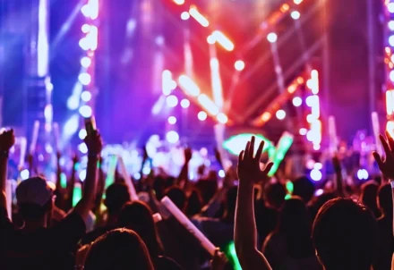 Crowd with raised hands at a colorful music concert.