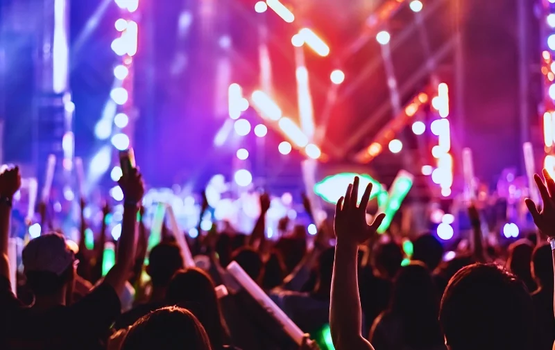 Crowd with raised hands at a colorful music concert.