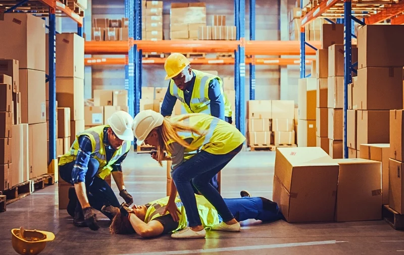 Workers attend to an injured colleague in a warehouse.
