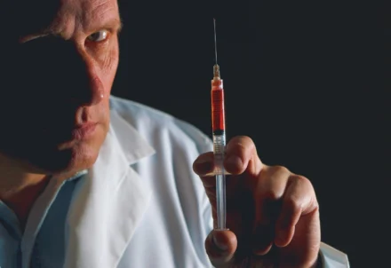 A man in a lab coat holding a syringe.