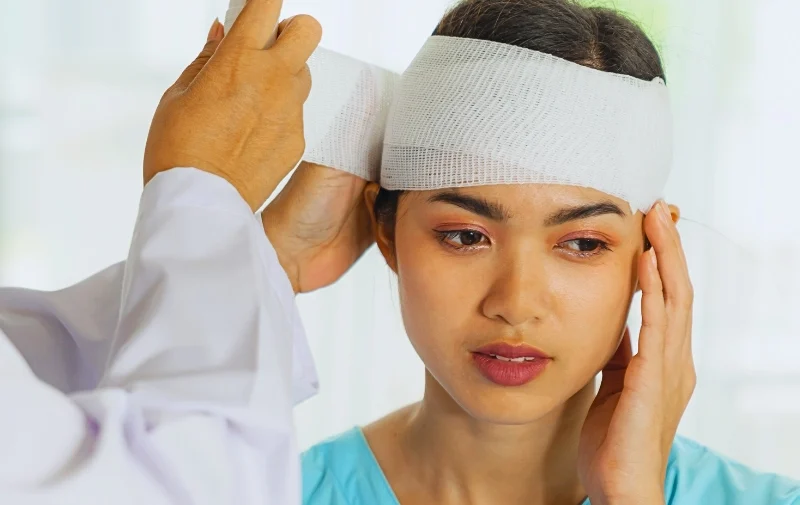 A healthcare worker wrapping a gauze bandage around a woman's head.
