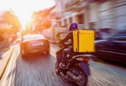 Delivery person on scooter speeds through city traffic.