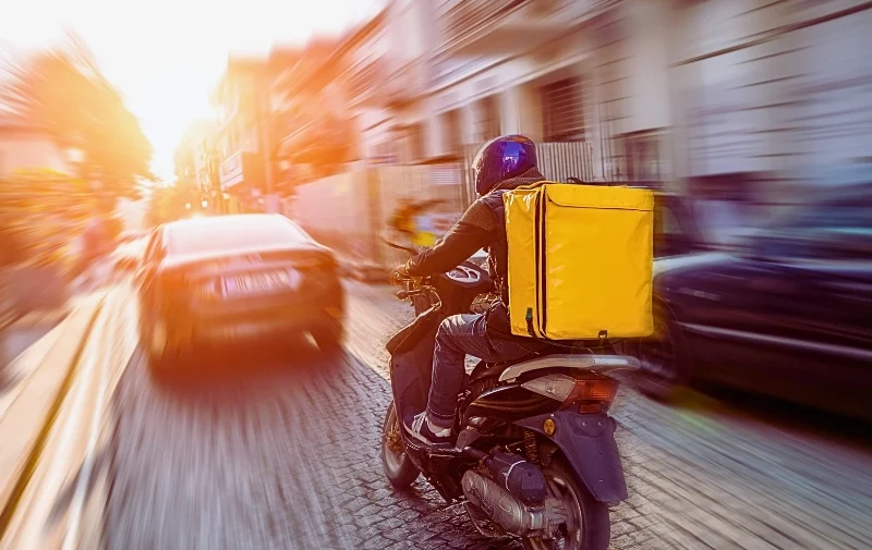 Delivery person on scooter speeds through city traffic.
