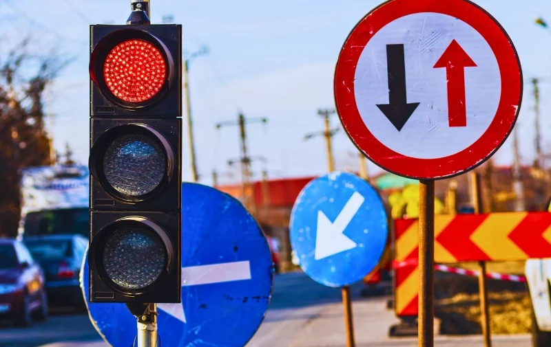 Red traffic light and various road signs on street.