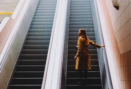 Woman in a tan trench coat standing on an escalator.