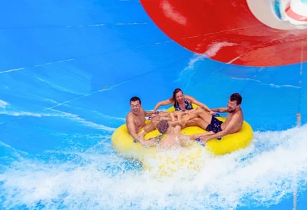 Four people cheering on a yellow water slide raft.