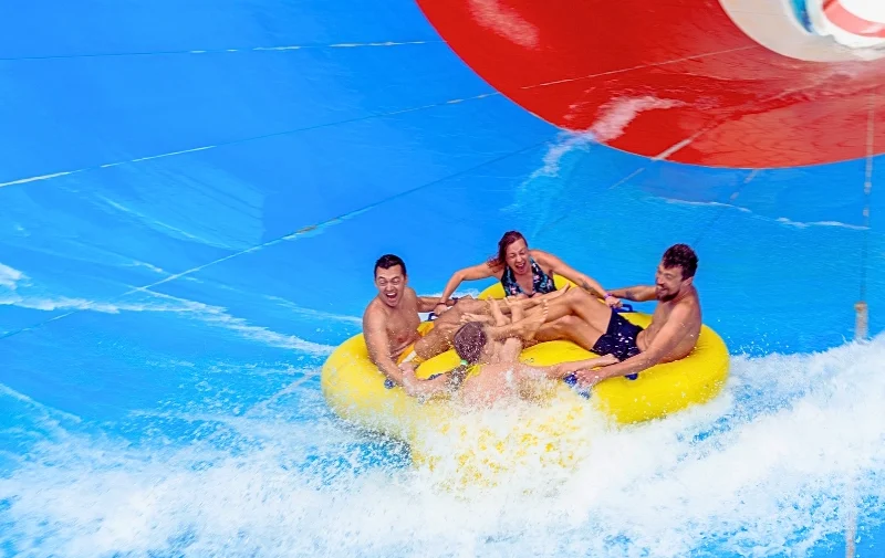 Four people cheering on a yellow water slide raft.