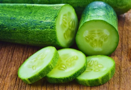 Sliced and whole green cucumbers on a wooden surface.