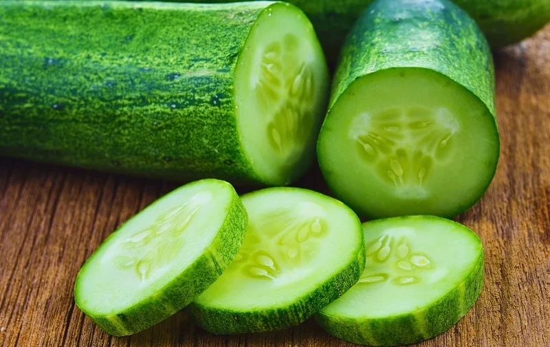 Sliced and whole green cucumbers on a wooden surface.