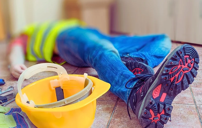 Construction worker lies injured on floor next to helmet.