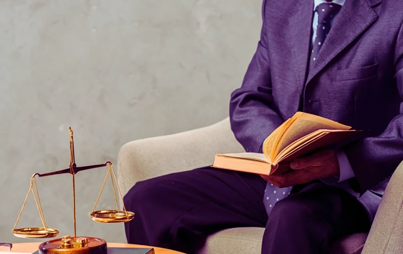 A lawyer reads a book next to justice scales.