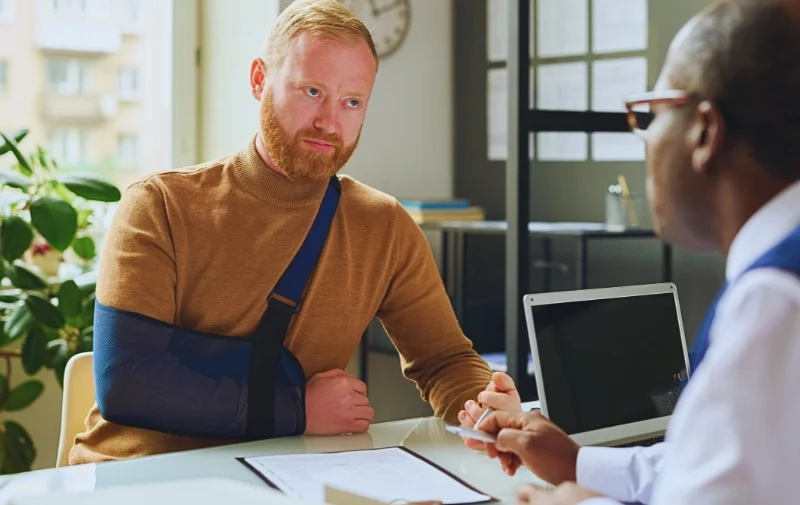 Injured man with arm sling meeting with an advisor. Your Employer Says Your Injury Is “Pre-Existing”