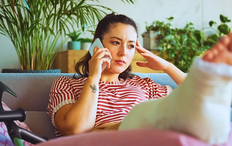 Woman with a cast on her leg talking on phone. workers' compensation claim is denied