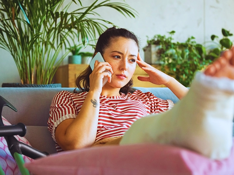 Woman with a cast on her leg talking on phone. workers' compensation claim is denied